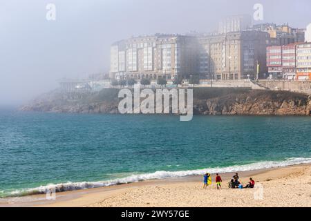 Strand von Orzán, Atlantik, Uferpromenade und die Gebäude von La Coruña bei starkem Nebel. Sonniger Tag. La Coruña, Galicien, Spanien. Stockfoto