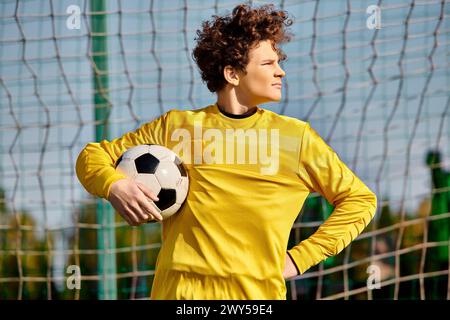 Ein Mann in einer leuchtend gelben Uniform hält selbstbewusst einen Fußball und strahlt Leidenschaft und Geschick für den Sport aus. Stockfoto