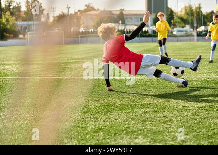 Ein kleiner Junge mit einem entschlossenen Ausdruck, der einen Fußball über ein riesiges grünes Feld kickt und seine Leidenschaft und sein Können für den Sport zum Ausdruck bringt. Stockfoto