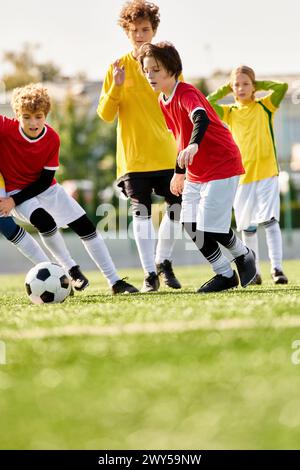 Eine Gruppe begeisterter Kinder verschiedenen Alters, die auf einem grasbewachsenen Feld Fußball spielen, den Ball treten, laufen und lachen, während sie ein freundliches G genießen Stockfoto