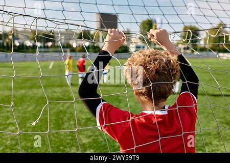 Ein kleiner Junge steht selbstbewusst vor einem Fußballnetz und ist bereit, sich entschlossen und zielgerichtet gegen eintreffende Schüsse zu verteidigen. Stockfoto