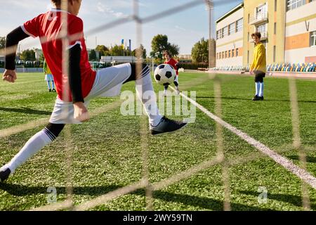 Eine lebhafte Gruppe von Kindern in bunten Trikots spielt auf einem sonnendurchfluteten Feld Fußball, jagt den Ball, dribbelt, vorbei und schießt in Richtung provisorischer goa Stockfoto