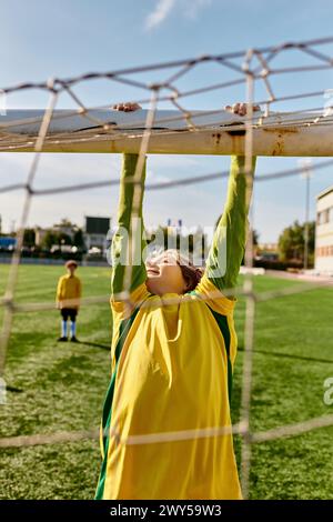 Ein kleiner Junge in einem leuchtend gelb-grünen Outfit greift freudig nach oben, um einen Fußball zu sehen, der mit eifriger Erwartung auf ihn zufliegt. Stockfoto