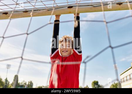 Ein talentierter Junge in einem leuchtend roten Hemd spielt begeistert Fußball und tritt den Ball mit Präzision und Geschick auf einem grünen Rasenfeld. Stockfoto