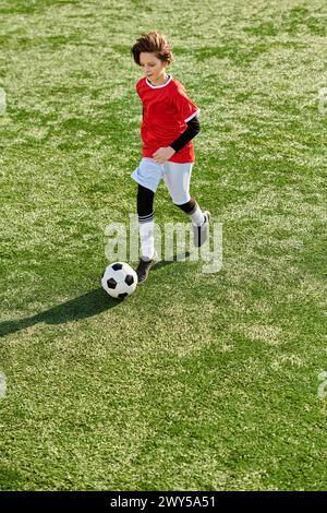 Ein kleiner Junge tritt mit Entschlossenheit und Geschick auf einem grünen Feld einen Fußball und zeigt seine Leidenschaft für den Sport. Stockfoto