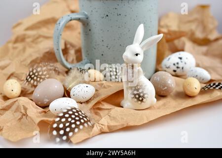 Osterkomposition mit weißem Kaninchen, Eiern und Federn auf braunem Kraftpapierhintergrund. Osterstillleben Stockfoto