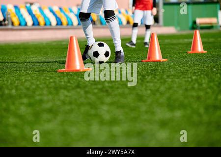 Ein erfahrener Fußballspieler tritt geschickt durch eine Reihe von orangen Kegeln, die in einer Trainingsübung aufgestellt werden. Die Spieler konzentrieren sich, Agilität und c Stockfoto