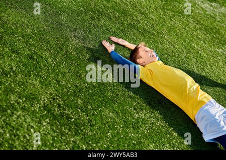 Ein kleiner Junge in einer Fußballuniform liegt friedlich auf dem Gras, starrt mit einem Lächeln auf dem Gesicht in den Himmel, verloren in Gedanken an das schöne Spiel. Stockfoto