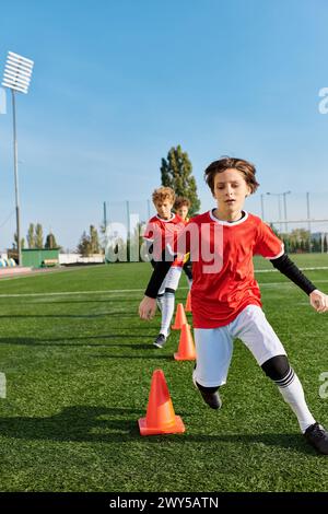 Ein fokussierter kleiner Junge kickt einen Fußball energisch um die Kegel und zeigt seine Agilität und Präzision bei der Ballkontrolle während eines Trainings. Stockfoto