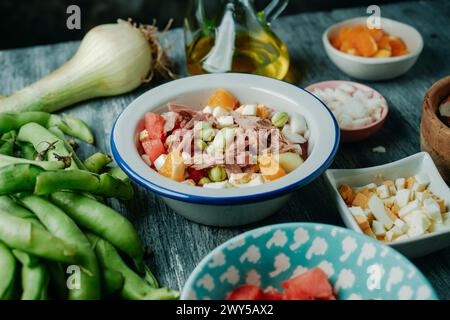 Nahaufnahme eines für andalusien typischen Salats mit breiten Bohnen, zubereitet mit Tomaten, Zwiebeln, gekochten Ei, Thunfisch und Orange, auf einem rustikalen grauen Holztisch Stockfoto