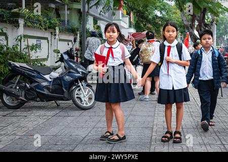 Kleine Kinder in der Schule während der Unterrichtsferien. Junge vietnamesische Schulmädchen auf der Straße. Kinder in vietnamesischer Schuluniform mit roter Krawatte. Ed Stockfoto