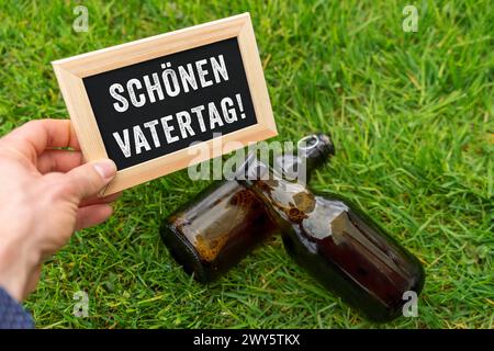 4. April 2024: Ein großer Vatertag-Mann hält einen Vatertag-Gruß auf einem Brett vor einer grünen Wiese mit Bierflaschen. FOTOMONTAGE *** schöner Vatertag Mann hält auf einer Tafel einen Gruß zum Vatertag vor einer grünen Wiese mit Bierflaschen. FOTOMONTAGE Stockfoto