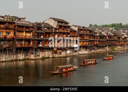 Touristenboote passieren die alten Holzgebäude am Ufer des Flusses in Fenghuang, einer antiken Stadt in Hunan, China. Mai 2008. Stockfoto