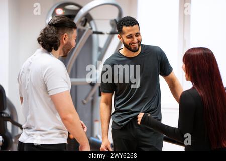 Eine fröhliche Gruppe von zwei Männern und einer Frau, die sich in einem Fitnessstudio unterhalten. Stockfoto