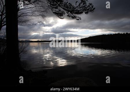 Loch Garten, Abernathy, Nethybridge, Aviemore, Cairngorm National Park, Schottland bei Sonnenuntergang mit Lichtstrahlen, die durch Wolken kommen, die sich auf See spiegeln Stockfoto