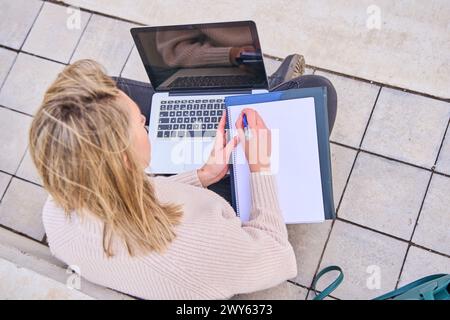 Student sitzt auf dem Boden mit einem Laptop und macht Hausaufgaben, Blick von oben Stockfoto