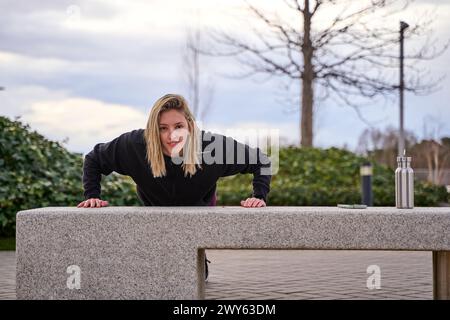 Junge Sportlerin, die Liegestütze auf einer Bank macht. Training auf der Straße. Stockfoto