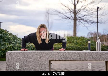 Eine junge Frau, die Bizeps-Liegestütze auf einer Straßenbank macht Stockfoto