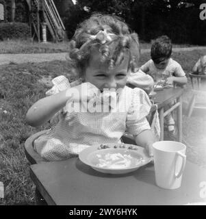 KINDERGARTEN: LEBEN IM ALTEN HERRENHAUS, WENDOVER, BUCKINGHAMSHIRE, ENGLAND, 1944 - Ein junges Mädchen, Maureen Pennington, versteckt sich in einer Schüssel mit Essen im Garten des Kindergartens im alten Herrenhaus in Wendover. Der Originaltitel besagt, dass die Kindermahlzeiten, wann immer möglich, im Freien serviert werden. , Stockfoto