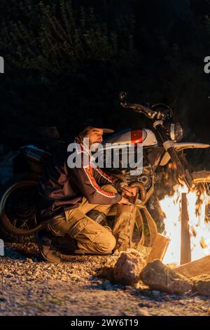 Eine Person sitzt am Feuer neben einem Motorrad Stockfoto