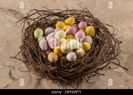 Bunte, zuckerüberzogene Mini-Eier, die in einem künstlichen Vogelnest angeordnet sind. Stockfoto