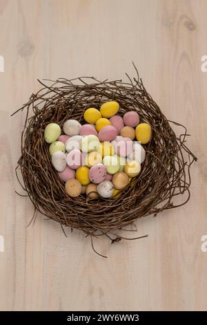 Draufsicht mit farbenfrohen, zuckerüberzogenen Mini-Eiern, die in einem künstlichen Vogelnest angeordnet sind. Stockfoto