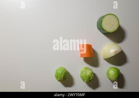 Gemüsestücke isoliert auf weißem Tischhintergrund. Gesundes Bio Rohgemüse von oben. Zucchini, rosenkohl, Zwiebeln, Karotten. Stockfoto