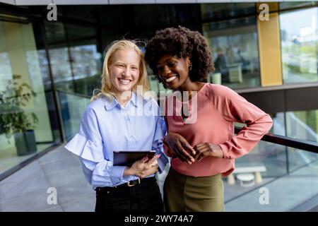 Zwei Frauen mit ähnlichen Merkmalen stehen nebeneinander, lächelnd, vor der großen Architektur. Stockfoto