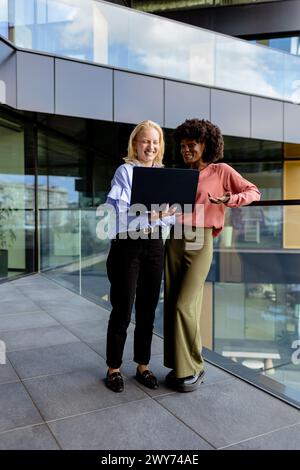 Zwei Frauen mit ähnlichen Merkmalen stehen nebeneinander, lächelnd, vor der großen Architektur. Stockfoto