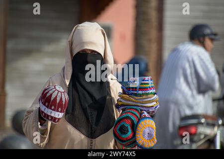 Eine Frau arabischer Herkunft, die ihr Gesicht mit dem Schleier bedeckt und bunte handgefertigte Wollmützen auf den Straßen von Marrakesch in Marokko verkauft Stockfoto