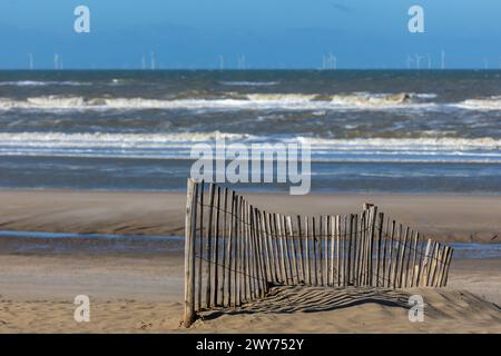 Ein verblasster Zaun am Strand der Nordsee in der Nähe von Egmond aan Zee, Niederlande, vor einem rauen Meer mit spindriftwellen Stockfoto