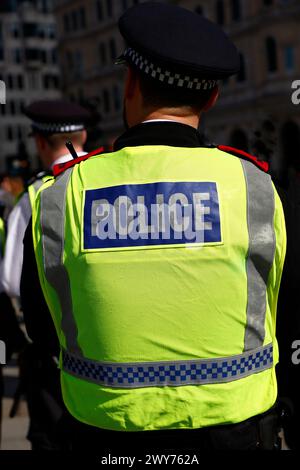 Nahaufnahme der Rückseite eines Polizeibeamten von der Taille aufwärts in einer gelben Jacke mit silbernen Streifen. Das Wort Polizei in großen weißen Buchstaben in einem blauen Rechteck. Draußen. Stockfoto