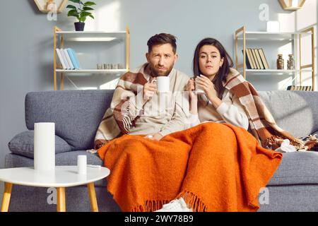 Mann und Frau sind zu Hause im Wohnzimmer, in warme Decke gewickelt und fühlen Grippesymptome. Stockfoto