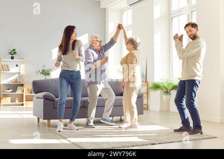 Glückliche Familie im Wohnzimmer alte Eltern Erwachsene Tochter und Sohn tanzen freudig. Familiäre Atmosphäre, altes Seniorenpaar und Kinder tanzt gerne Stockfoto