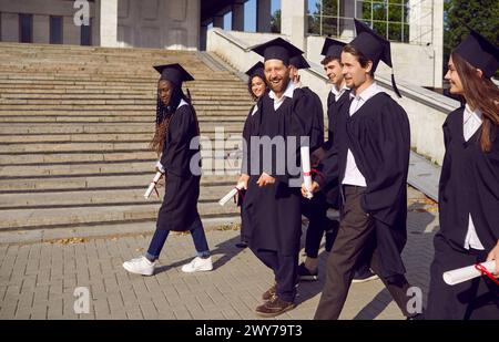 Eine Gruppe glücklicher Absolventen verschiedener Universitäten, die am Abschlussfeiertag über den Campus laufen Stockfoto