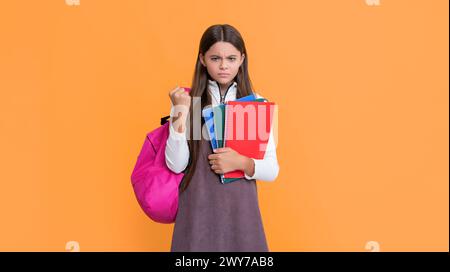 Wütendes Kind mit Schulrucksack und Arbeitsbuch auf gelbem Hintergrund. Stockfoto