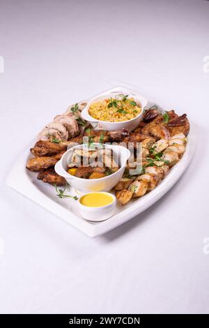 Verschiedene gebratene Fleischsorten, buntes Gemüse und goldene Kartoffeln garniert mit frischer Petersilie und herzhaften Saucen auf einer weißen Platte. Stockfoto