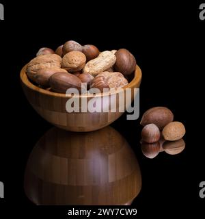Verschiedene Nüsse in einer Holzschale und drei Nüsse, die in einer kleinen Gruppe auseinander liegen Stockfoto