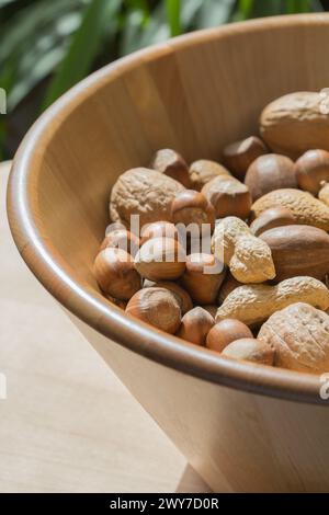 Verschiedene Nüsse in einer großen Holzschüssel auf einem blattgrünen Hintergrund Stockfoto