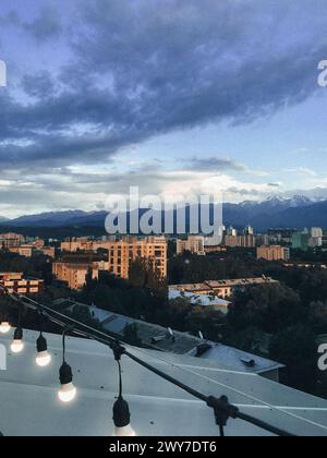 Eine atemberaubende Stadtlandschaft mit Bergen im Hintergrund, umgeben von grünen Bäumen unter einem blauen Himmel mit weißen Wolken. Stockfoto