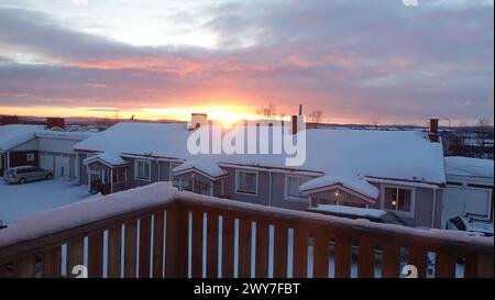 Sonnenaufgang in einer kleinen verschneiten Stadt im Norden Schwedens. Die Sonne geht über den Dächern auf. Stockfoto