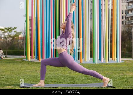 Ein wunderschönes blondes Model und Yogalehrerin, das Yoga im CityLife Park vor der Coloris Skulptur CityLife, Mailand, Italien macht Stockfoto