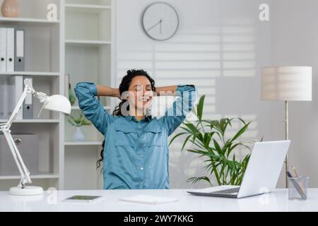 Eine junge Geschäftsfrau mit geschlossenen Augen lehnte sich zurück in ihren Stuhl und machte eine entspannende Pause an ihrem Arbeitsplatz in einem hellen Büro. Stockfoto