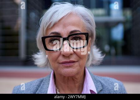 Porträt einer Reifen kaukasischen Geschäftsfrau mit Brille und weißem Haar im formalen Anzug lächelnd Stockfoto