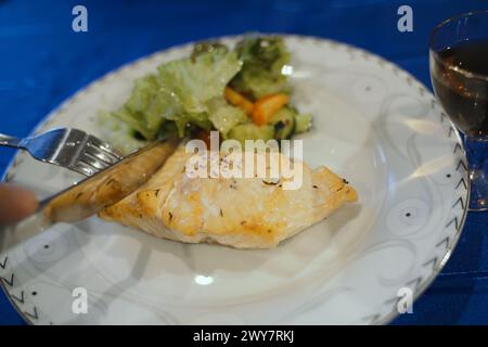 Ein Stück gegrillter Lachs, gewürzt mit Kräutern auf einem weißen Teller, begleitet von einem frischen grünen Salat, bereit für eine gesunde Mahlzeit. Stockfoto