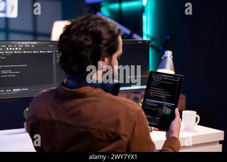 Ein Mann, der die Software-Qualitätssicherung mit einem Tablet durchführt und den Quellcode vor der Implementierung liest. Programmierer überprüft die Codierung auf einem tragbaren Gerät, um potenzielle Fehler zu beheben Stockfoto