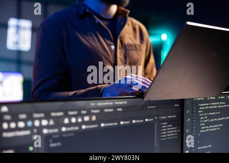 Freiberuflicher IT-Administrator, der von zu Hause aus mit Laptop arbeitet, Programme testet und implementiert. Softwaretechniker überprüft den Code, der auf Computerdisplays angezeigt wird, stehend in der Wohnung, Nahaufnahme Stockfoto