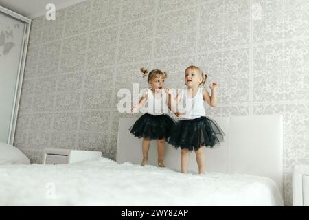 Zwei junge Mädchen in lässiger Kleidung springen glücklich auf ein Bett in einem Schlafzimmer. Stockfoto