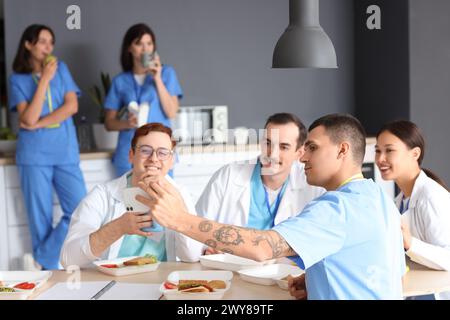 Ärzteteam nimmt Selfie beim Mittagessen am Tisch in der Krankenhausküche Stockfoto