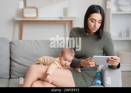 Junge Frau mit Tablet-Computer und ihr Baby, das zu Hause an postnataler Depression leidet Stockfoto